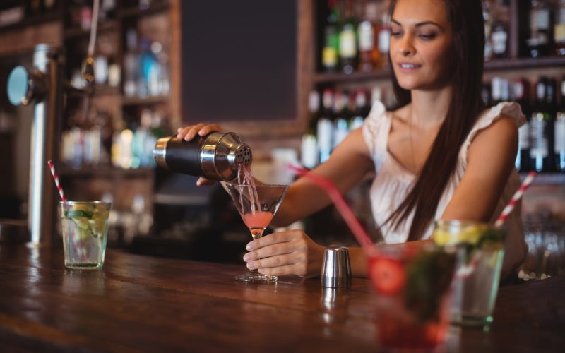 Female bartender pouring cocktail drink in the glass at bar counter